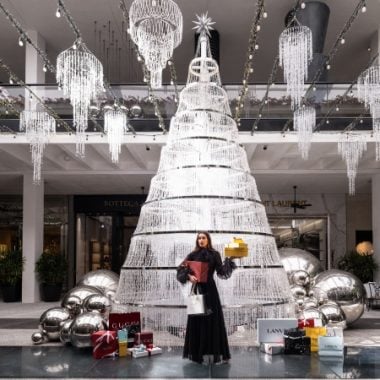 Model-wearing-black-dress-in-front-of-crystal-tree-boxes-and-shopping-bags