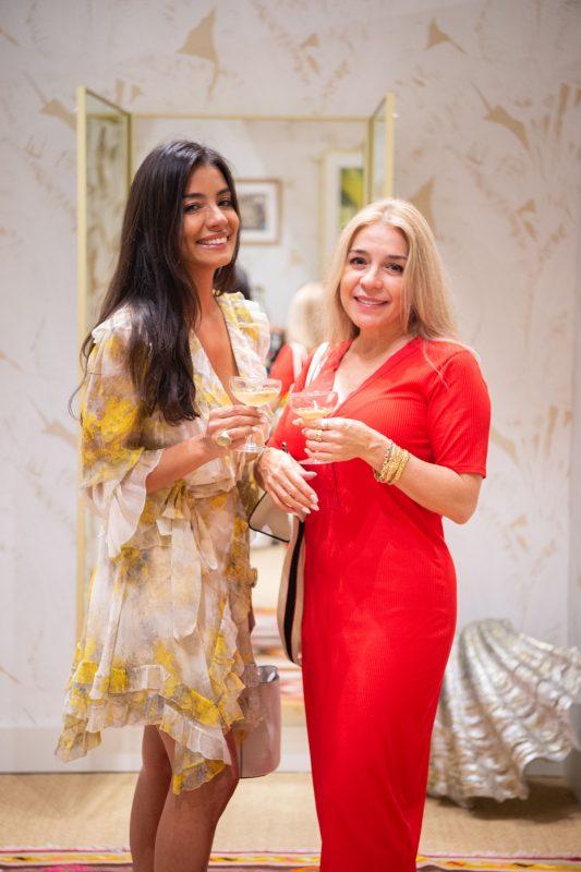 Two women pose for a photo while smiling and holding their cocktails