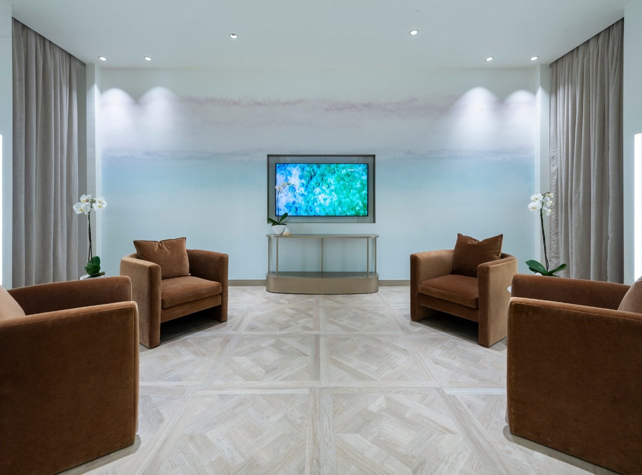 A room within the spa area at Neiman Marcus Bal Harbour Shops that has four brown chairs and TV screen