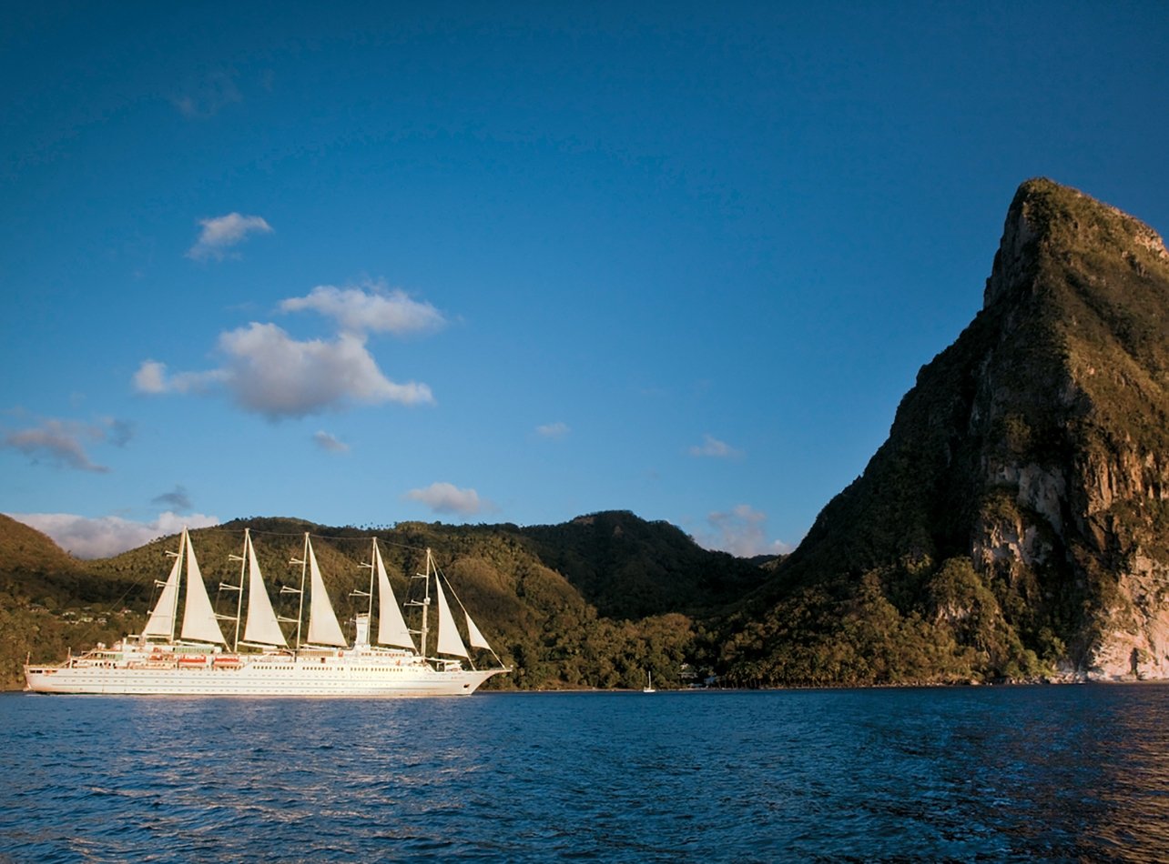 Windstar Cruises’ Wind Spirit cruising on ocean with green mountains in the distance