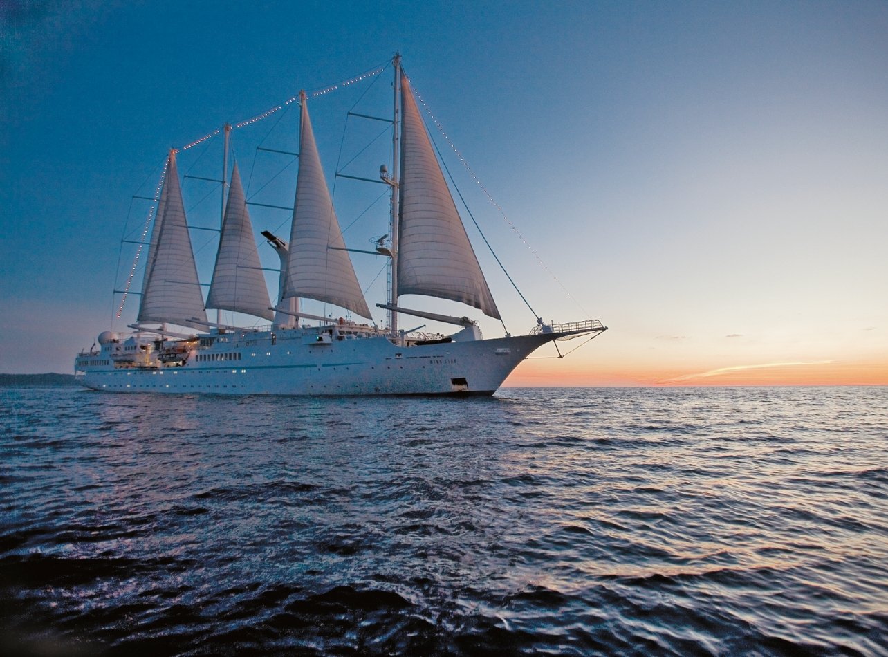 Windstar Cruises’ Wind Spirit sailing in ocean with sunset in the background