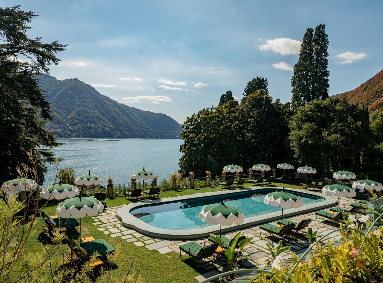 Pool with green and white umbrellas and lounge chairs surrounded by greenery and a view of the water