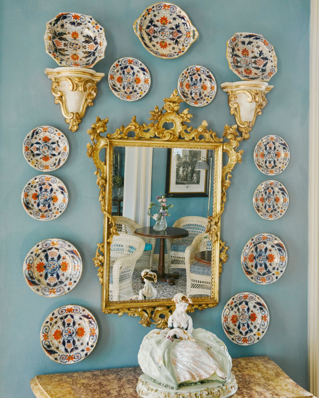 Blue painted wall with printed plates hanging and gold mirror