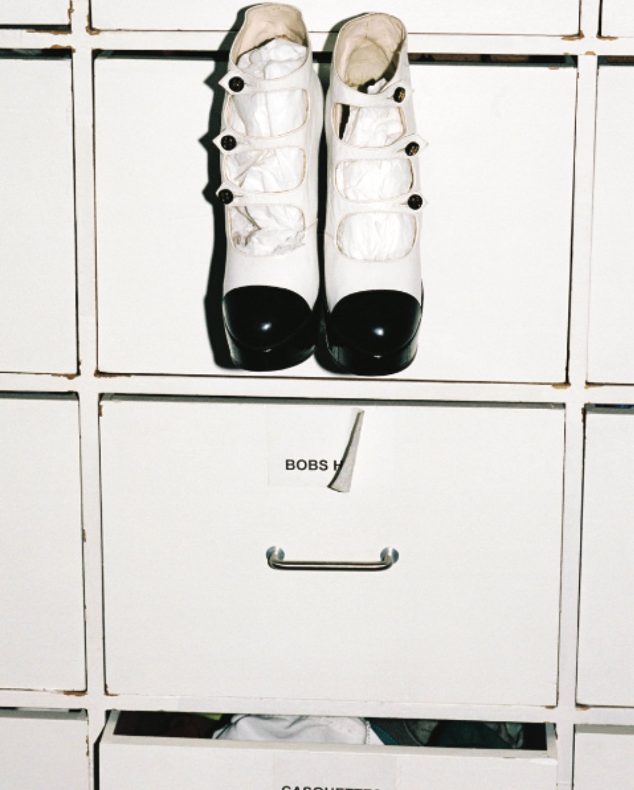 White and black shoes by Massaro for Chanel hanging out of white drawers