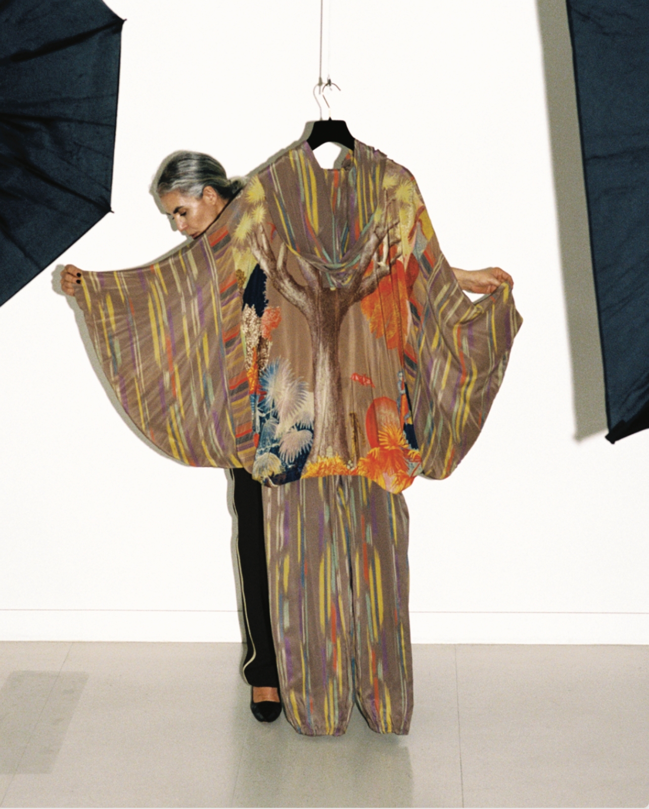 Zohra Alami holding a multicolored Issey Miyake dress that is hanging from the ceiling