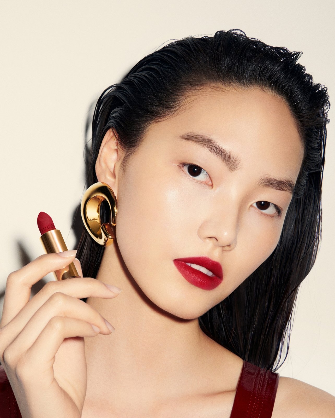 Model wearing red Gucci lipstick and holding an opened red lipstick with gold gucci earrings