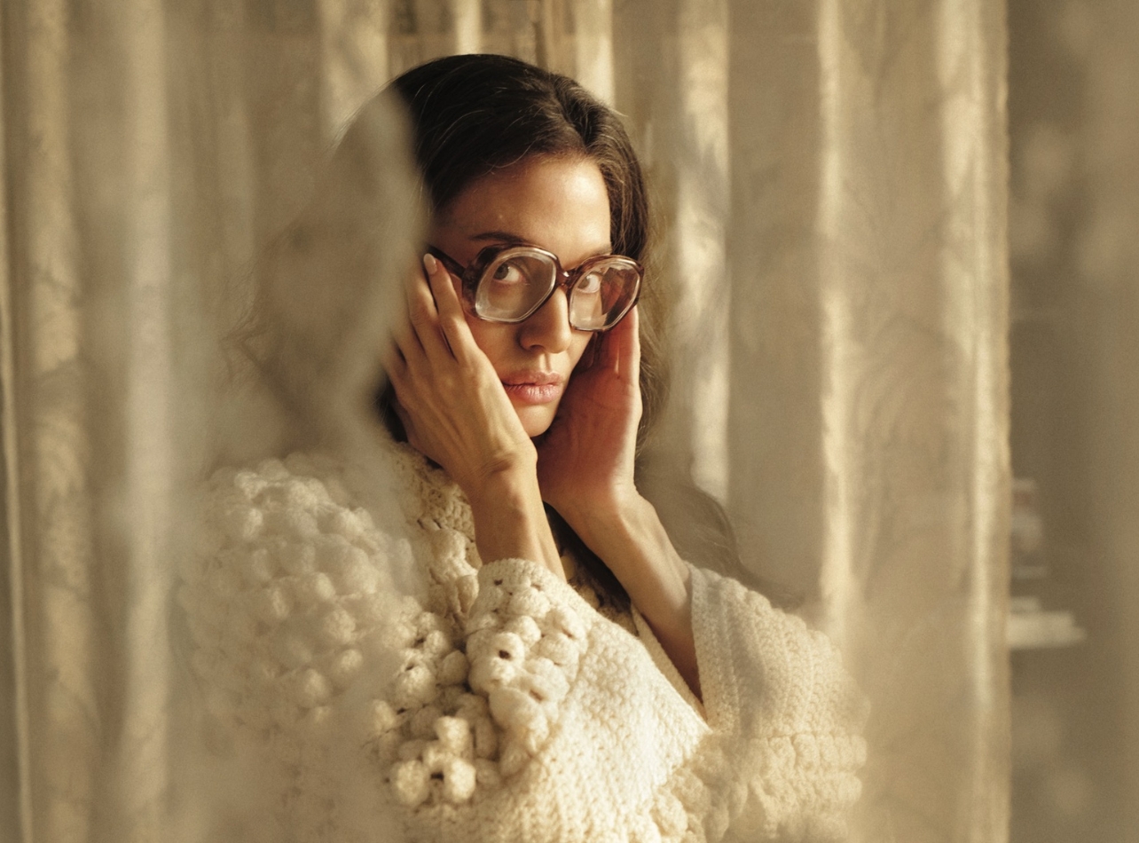 Angelina Jolie in a white sweater and glasses holding her face