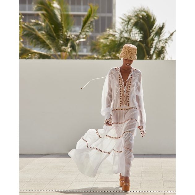 Model walking, wearing an Ermanno Scervino long white embroidered dress with a hat and platforms