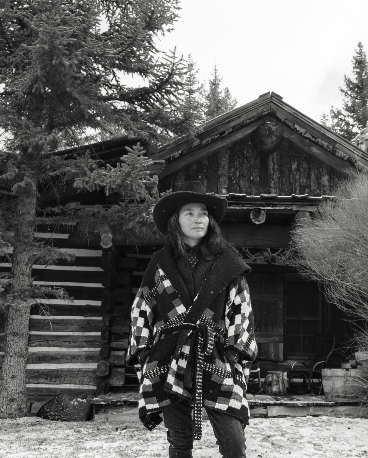 Black and white Portrait of a woman standing outside a log cabin