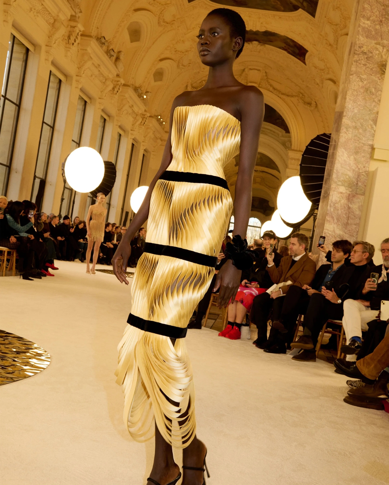 Schiaparelli model wearing gold dress with black suede lines