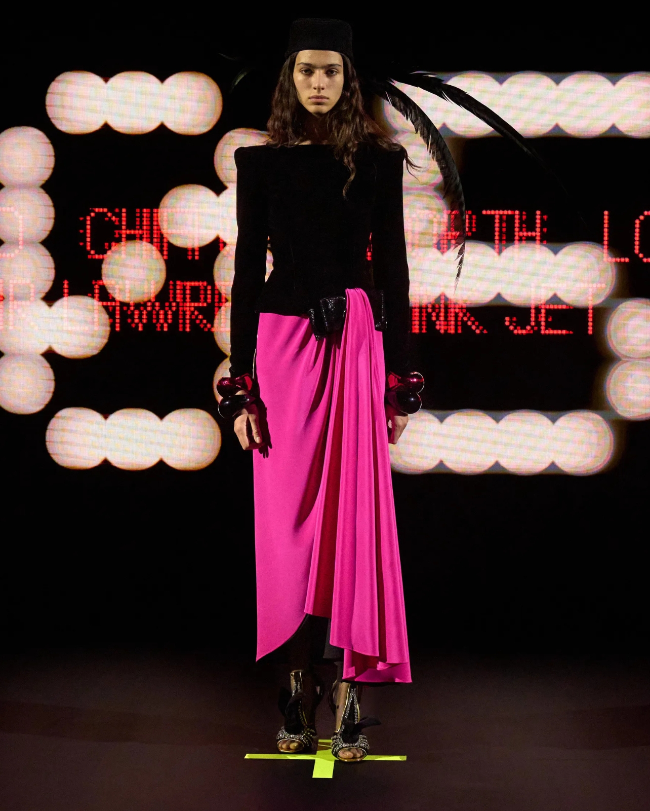 Valentino model wearing a hot pink and black dress with a black feather headpiece