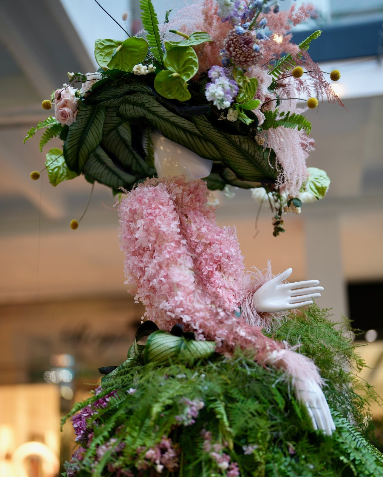 Mannequin wearing a hat made out of greenery and pink and lavender flowers with a dress made up of pink florals and greenery