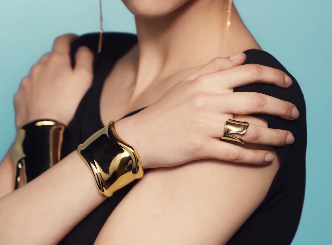 Blue background with models arms and hands with gold cuffs and ring