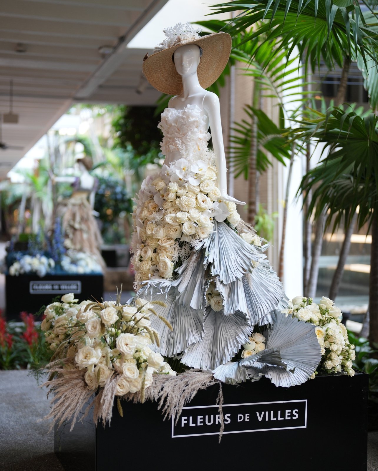 Mannequin of female with dress made up of a variety of while florals with a hat standing on a black pedestal