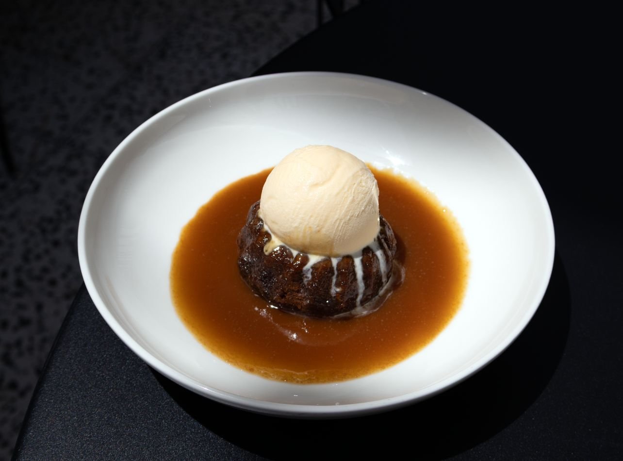 Plate of sticky toffee pudding with vanilla ice cream on top from The Whitman restaurant