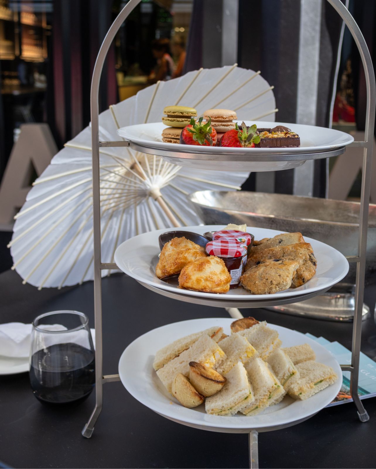 Table with high tea stand with white umbrella and glass of wine