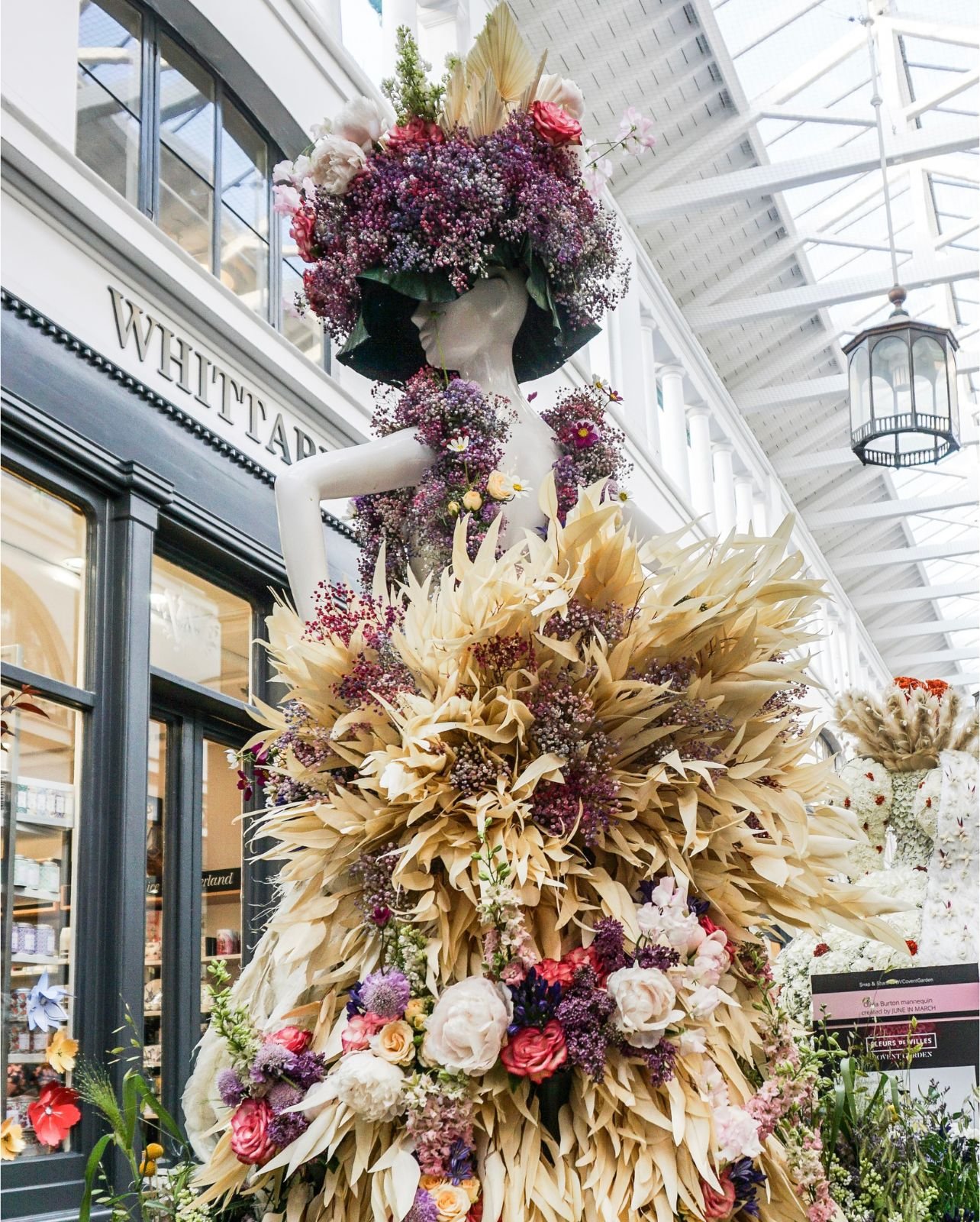 Mannequin wearing a dress made up of pink and purple flowers with cream colored leaves and a headpiece made up of purple and pink florals