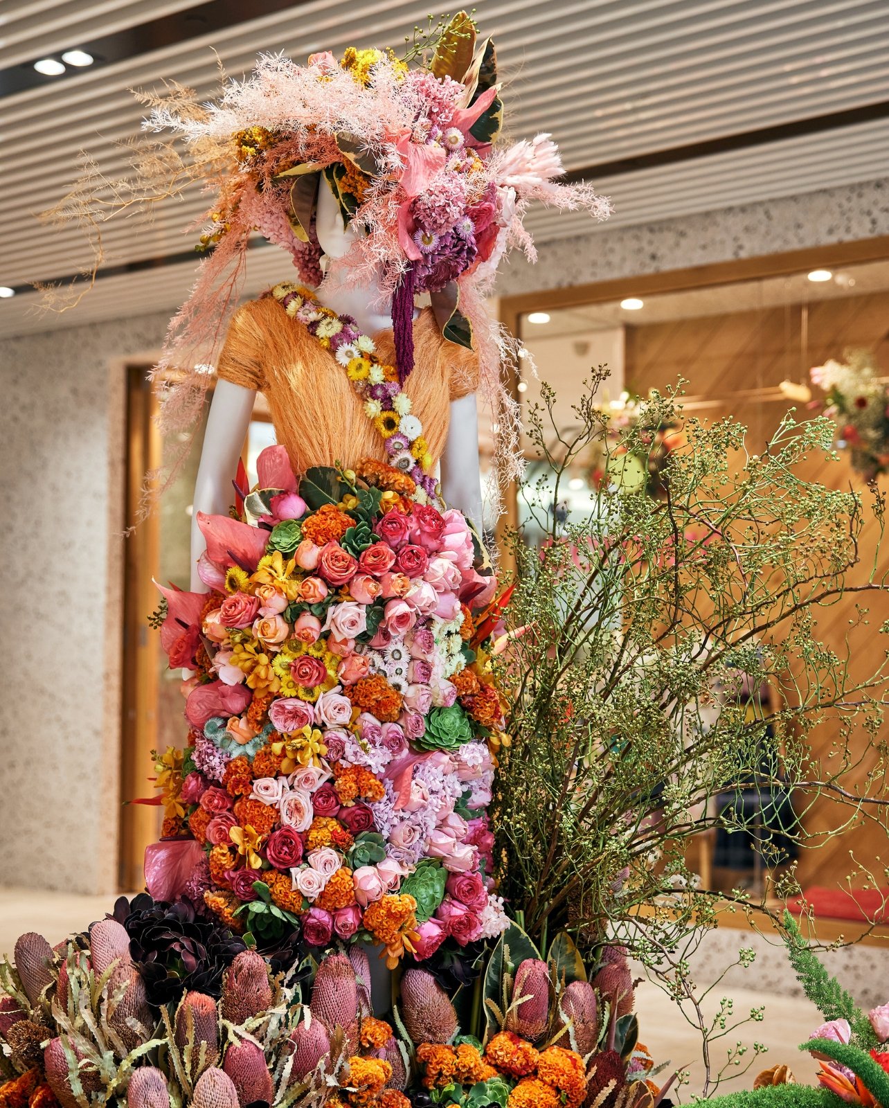 Mannequin of female with dress and hat made up of mulitcolored pink, yellow, orange and purple flowers with some greenery