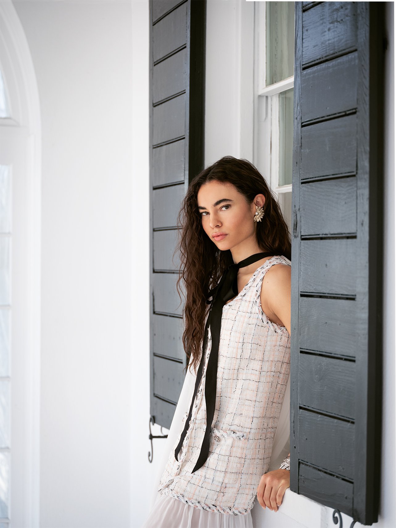 Model wearing Chanel tweed dress with black satin necktie standing in front of a window and black shutters