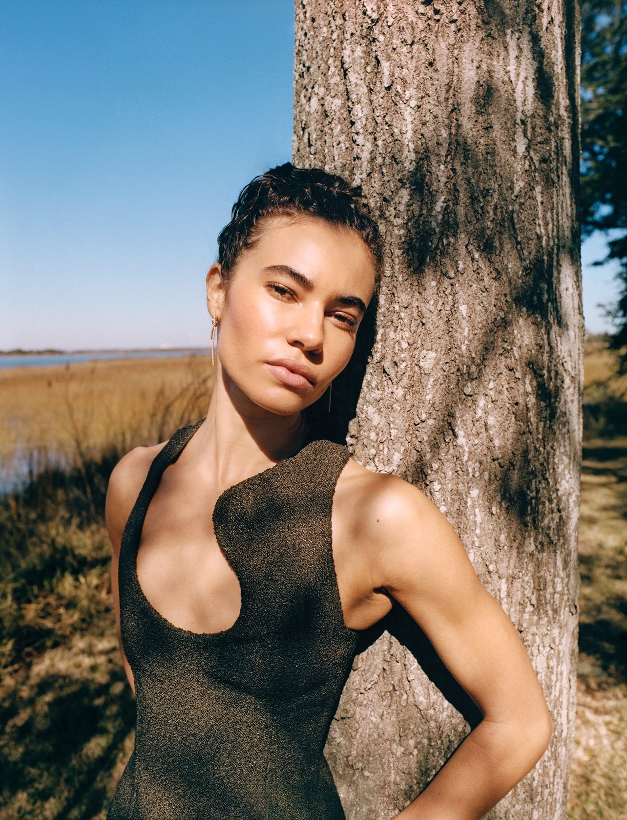 Model wearing a black Ferragamo dress and Tiffany & Co. earrings, leaning against a tree