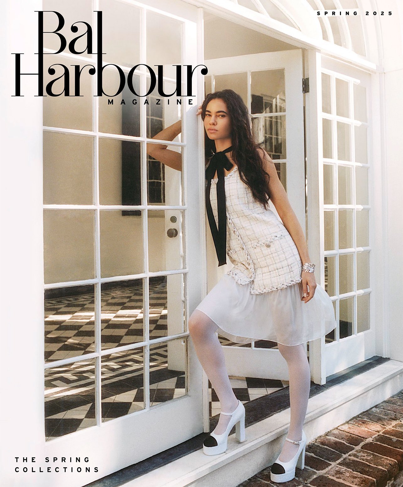 Model wearing a white and black Chanel dress with white tights, a black necktie and black and white platform heels, standing in between a white and glass doorway