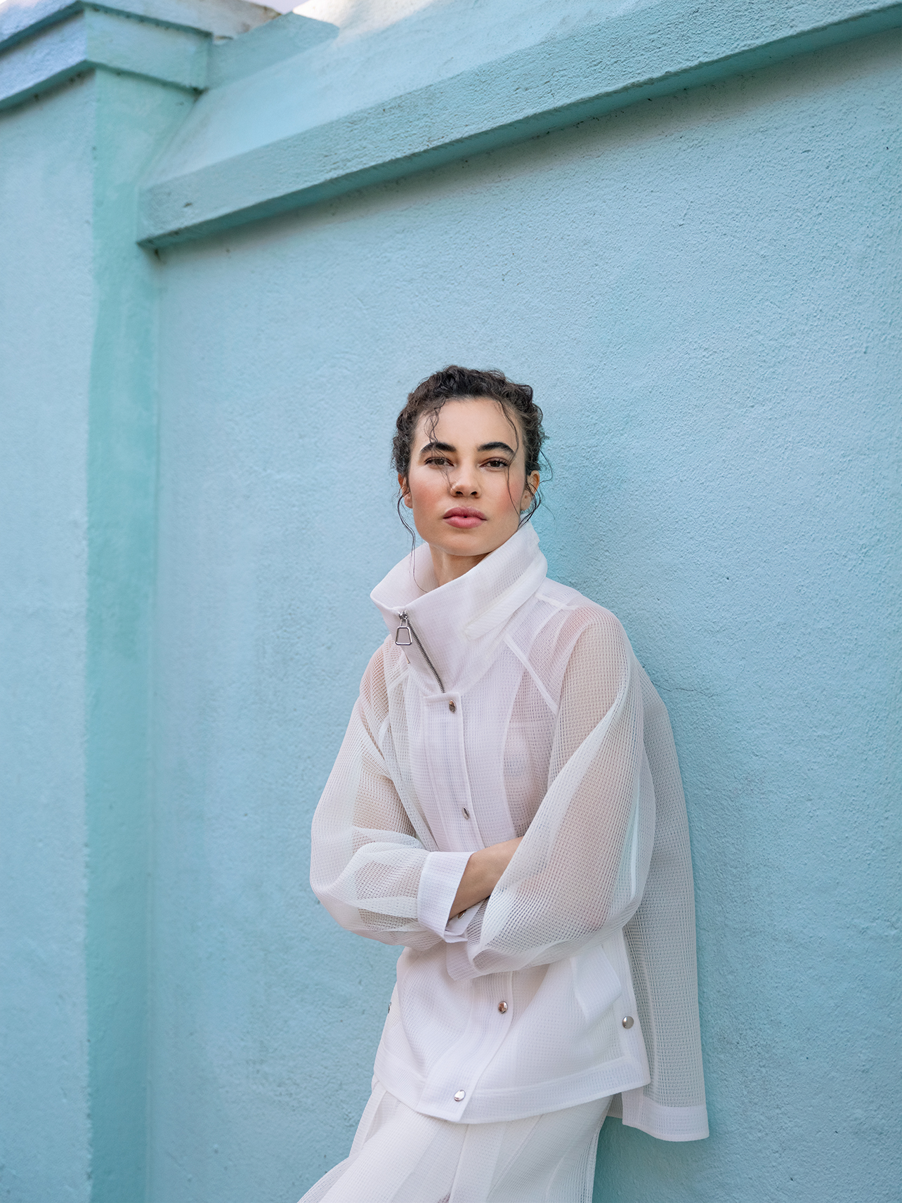 Model wearing an all white Akris outfit standing against a blue wall